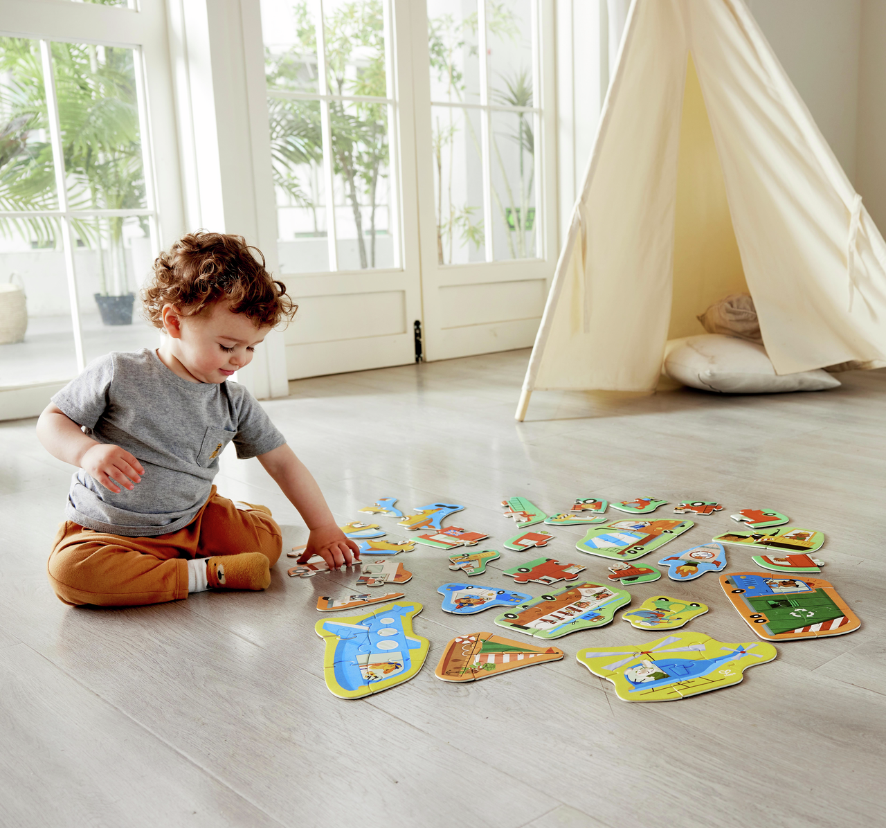 Niño montando puzzles de vehículos del set Hape Rompecabezas de Ruedas y Maravillas.